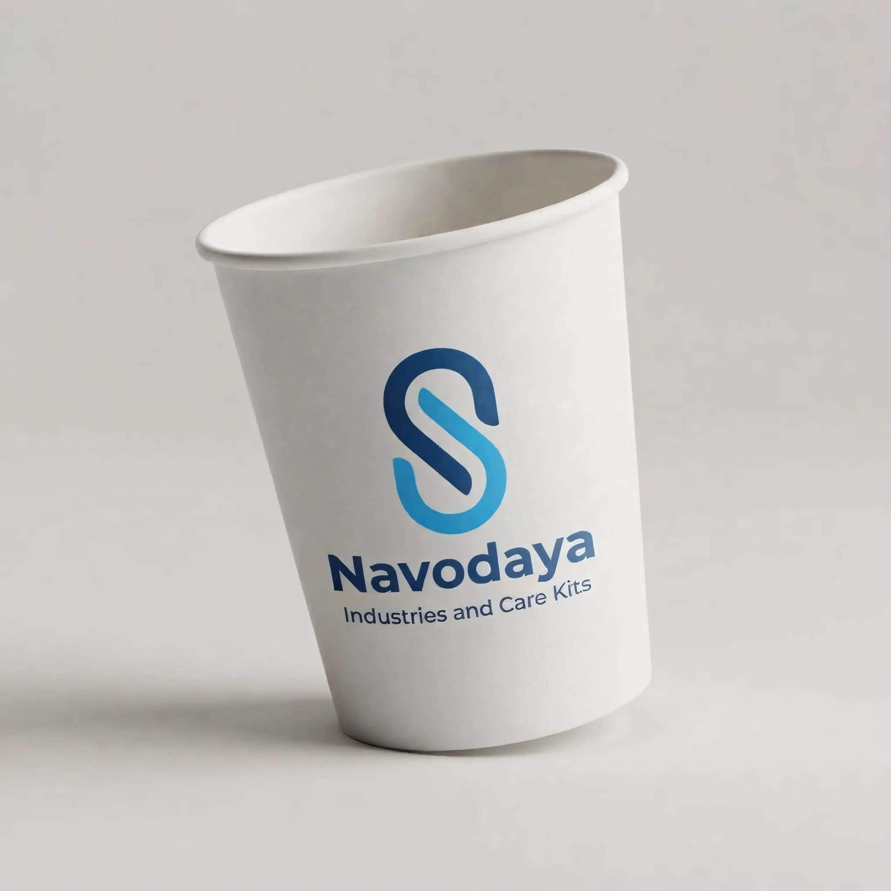 A white single-use paper cup photographed at a three-quarter angle on a plain pale ground, printed with the Navodaya logo and wordmark, showing the rolled rim and tapered wall
